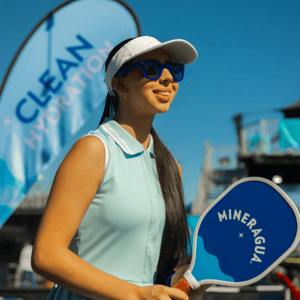 Woman in blue top and white hat playing pickleball